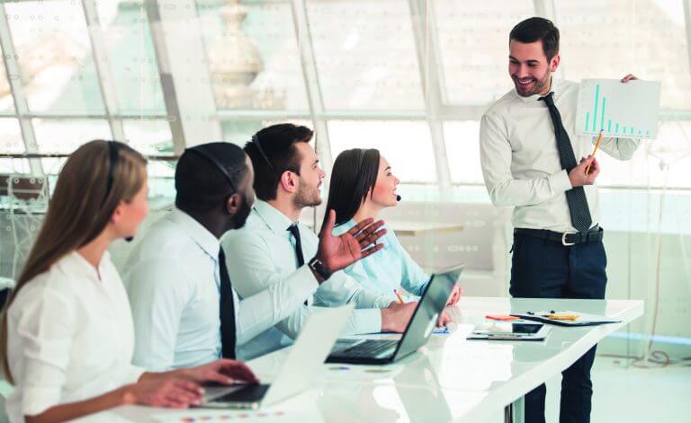 Attractive business people in suits and headsets are smiling and listening to their colleague while working with laptops in office